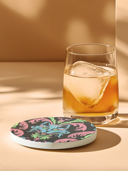 Circular ceramic coaster featuring a turquoise cat face with green eyes on black background, surrounded by pink scrollwork and green leaves in Victorian damask style.
